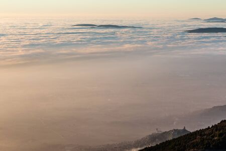 A view from above of Assisi town (Umbria, Italy) in the middle of mist, with beautiful, warm sunset colors.の写真素材