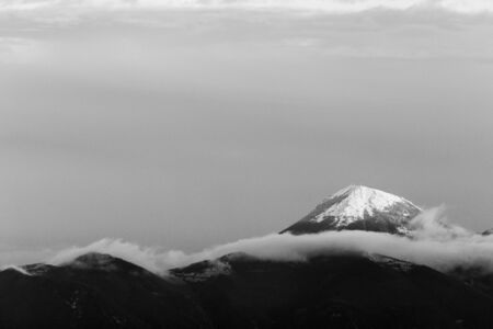 Mountain top covered by snow in the middle of cloudsの写真素材
