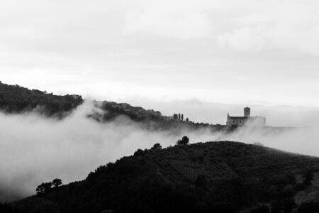 A view of St Francis church in Assisi (Umbria, Italy) veiled by fog, with an hill in the foregroundの写真素材
