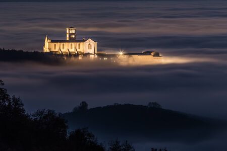 View of St.Francis church (Assisi, Umbria) at night, over a sea of fogの写真素材
