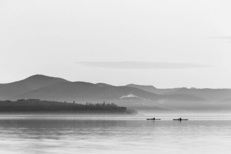 Beautiful view of a lake with two men on canoesの写真素材