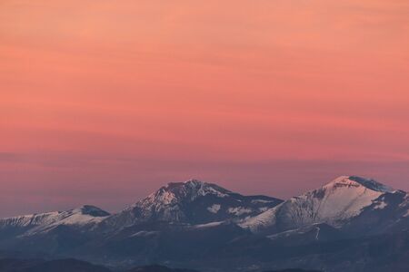 Mountain top covered by snow with a beautiful orange sky on the background