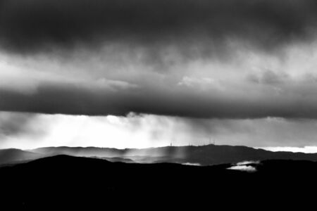 Sunrays coming over mountains beneath moody clouds.