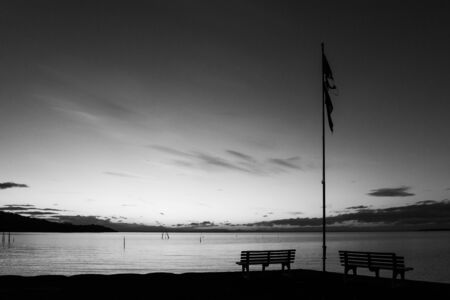Dusk at Trasimeno lake (Umbria, Italy), with a parking bench and a worn flag on the foreground.の写真素材