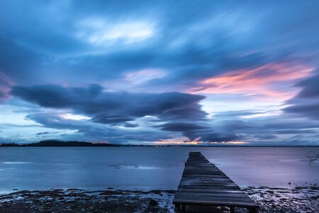 View of a pier on a lake at dusk, beneath a dramatic, moody skyの写真素材