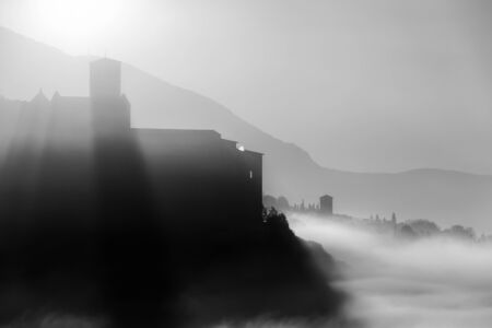 Surreal view of Assisi and St.Francis church (Umbria, Italy) in the middle of fog at dawnの写真素材