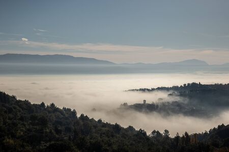 Surreal view of of a little town in Umbria (Italy) almost completely hidden by fog.の写真素材