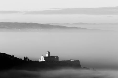 An epic view of St.Francis church in Assisi town (Umbria) above a sea of fog at dawnの写真素材