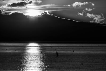 Sunset on Trasimeno lake (Umbria, Italy), with the sun coming down behind big clouds and beautiful water reflections.の写真素材