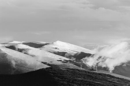 Mountain (Umbria, Italy) in winter, covered by snow, with low clouds and wind turbines.の写真素材