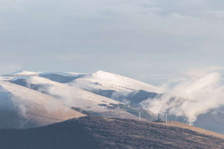 Mountain (Umbria, Italy) in winter, covered by snow, with low clouds and wind turbines