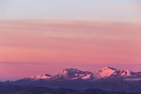 Mountain top covered by snow with a beautiful orange sky on the backgroundの写真素材