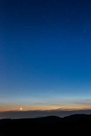 Moon and Neowise comet at dusk on a blue sky above mountains