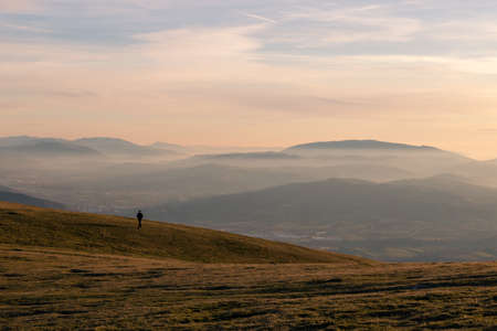 A distant man on a mountain at golden hour, with mist, fog and layers of mountains in the background. Umbria Italyの写真素材