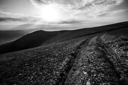 Sunset above mountains with a path in the foreground going away to the distance