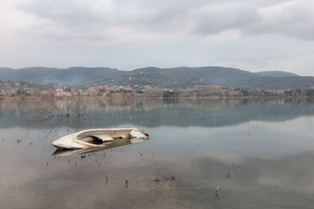 A sinking little boat on Trasimeno lake, Umbria, with Passignano town in the backgroundの写真素材