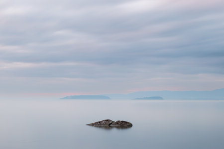 Long exposure view of a rock in Trasimeno lake Umbria, with islands in the background and moody skyの写真素材