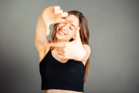 Girl in a black top with her hair taking pictures with her hands. On a gray background. Without makeup, without retouching.の写真素材