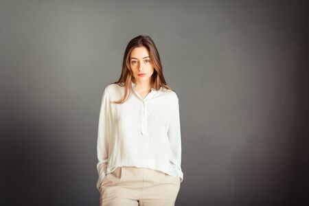 Young girl in a white shirt on a gray background. French woman in white blouse against a background of gray walls. Without retouching.の写真素材