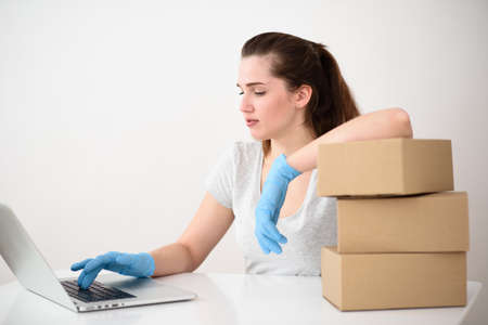 A girl sits at a table and laughs showing a finger at the screen with a stack of corton boxes on white izolate backgraundの写真素材