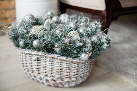Snow covered Christmas tree twigs with silver toys in a basket. Christmas composition in the interior view from the sideの写真素材