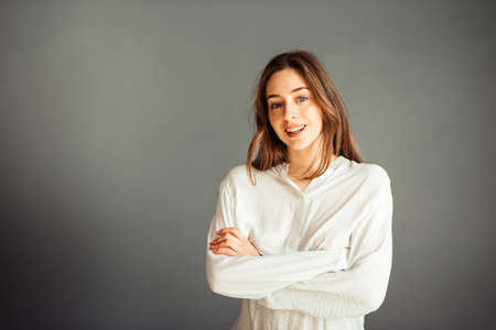 Young girl in a white shirt on a gray background. French woman in white blouse against a background...