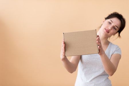 the girl with interest examines the box from the side on a beige background. present