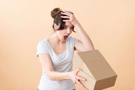 The girl holds a cardboard box at arm's length clutching her head.の写真素材