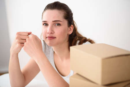 A beautiful girl with a heartfelt gentle look, folding her fists, sits in the center of the table behind brown boxesの写真素材
