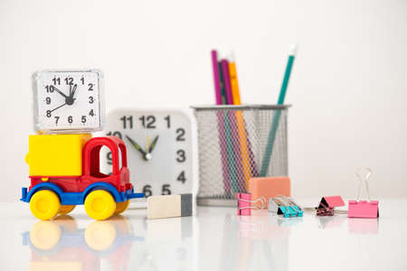 On the table in front of a clock and a glass of pencils is a toy car with a clock on top.