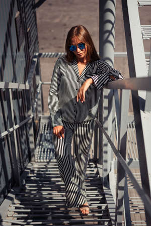 girl in glasses and loose suit climbs metal steps, leaning against railing. Photo from top to bottomの写真素材