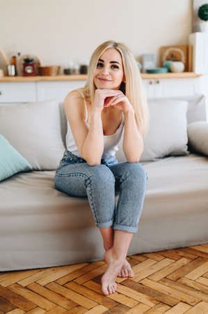Parquet in the kitchen. A girl in jeans and a T-shirt is sitting on the couch with her elbows on her...