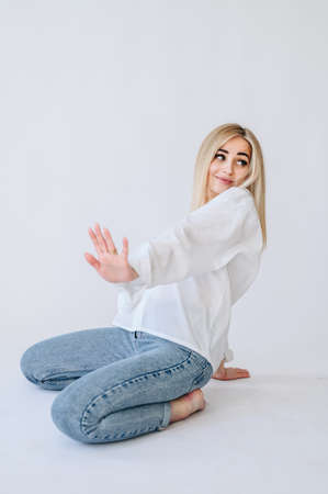 A girl in jeans and a white shirt put her hand forward and looks to the side. Girl on a white background in jeansの写真素材