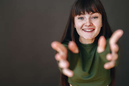 Close-up portrait of a young brunette woman with freckles on her face who reaches out for a hug. The...