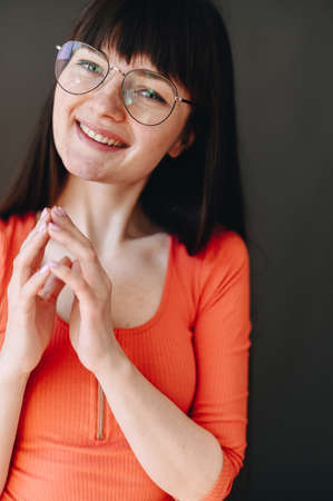 A close-up portrait of a smiling girl in glasses who folded her hands in front of her and looks playfully at the camera.の写真素材