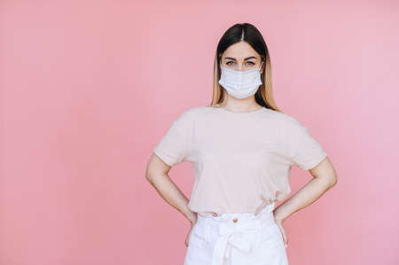 A girl in light casual clothes stands in a mask on a pink background. health concept.