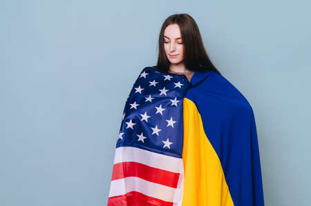 A girl with brown hair on a blue background with an American and Ukrainian flag. The concept of US support to Ukraine.の写真素材