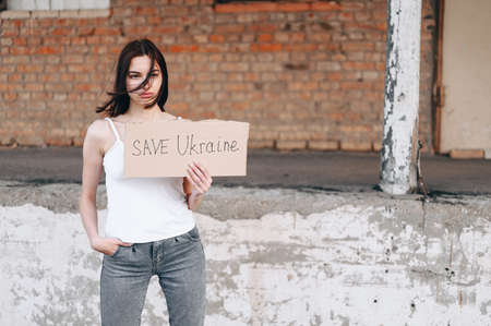 Ukrainian calls to stop the war in Ukraine. holds the sign Save Ukraine and looks with a tired and devastated look. Praying for peace.の写真素材