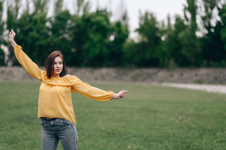 A girl in a yellow blouse spreads her arms to the side and looks into the distance, standing in the middle of a green meadow.の写真素材