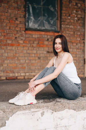 A smiling girl with a short haircut sits against the background of a full-length brick building....