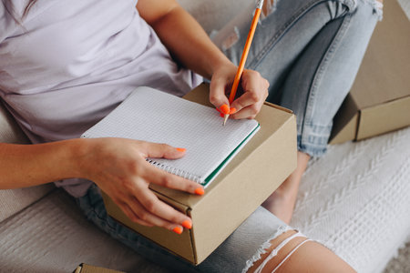 Close-up of hands that make notes in a notebook. Girl sitting on the couch makes notes top view.