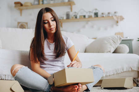 Close-up portrait of a girl who writes on a box in a home interior on the floor with a serious...
