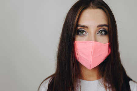 Close-up portrait of girl's face, look straight into camera, her mouth is covered with mask against...
