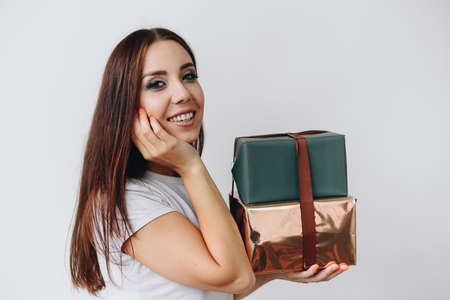 A large portrait of a girl stands sideways on a white background in her hands holding gifts,...