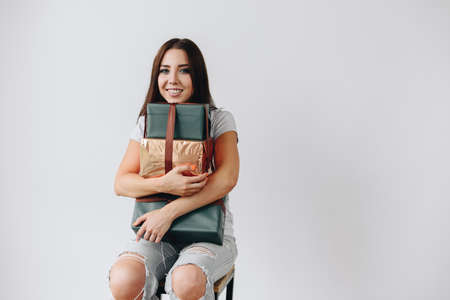 Satisfied Girl Sitting on a Chair Holding a Stack of Gifts in Her Hands Against the Background of a...