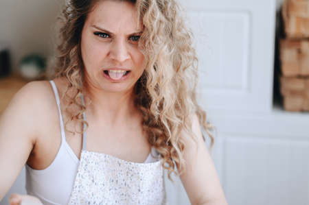 Horizontal Portrait of a Curly Housewife. Housewives with Disgusted Expression. Wife Sitting in the Kitchen and Sticking Out Her Tongue Close-up Portrait.の写真素材