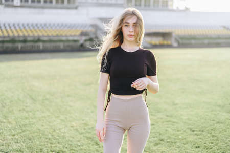 young girl stands at the stadium in the evening. Girl in black top and beige leggings. wind develops...