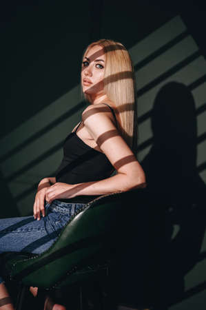 A self-assured woman sits sideways in a leather chair. A painted Blonde on a green background with...