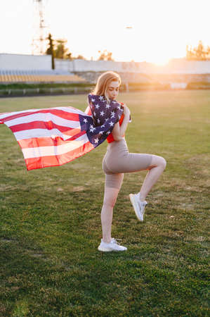 Vertical Photo of Girl with an American Flag at Sunset. Flag is Developing in Wind. Independence Day Conceptの写真素材