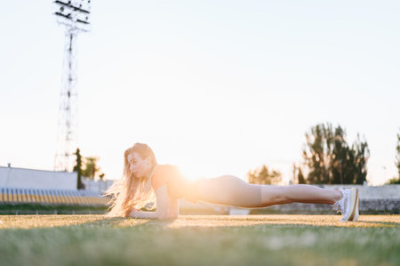 Young Girl Doing Physical Exercises Standing in Plank at Sunset. Exercising on Summer Evening. Lifestyle Against Sun Athletic Girl.の写真素材
